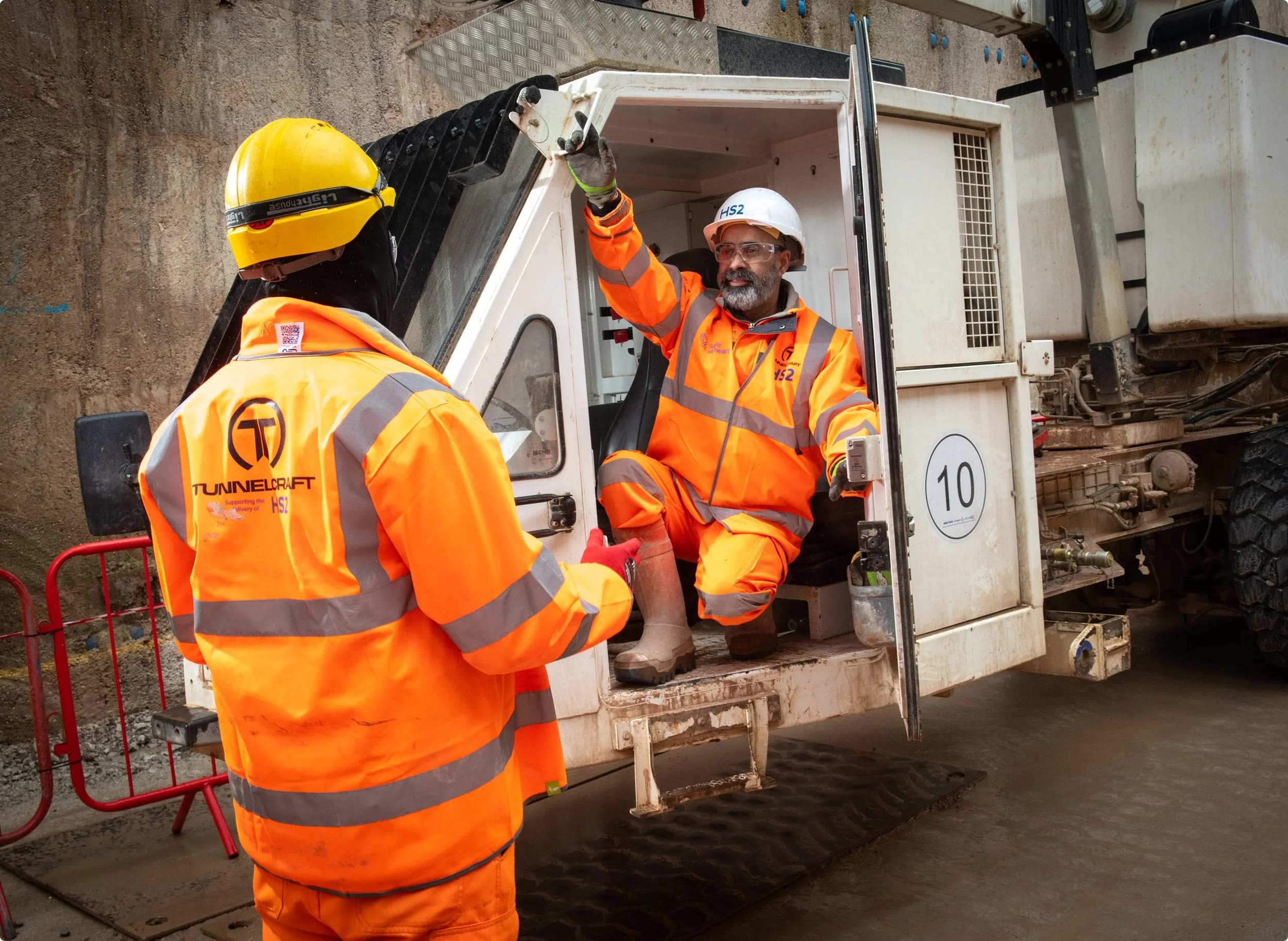 Tunnelcraft operatives in branded HS2 workwear talking at a site vehicle